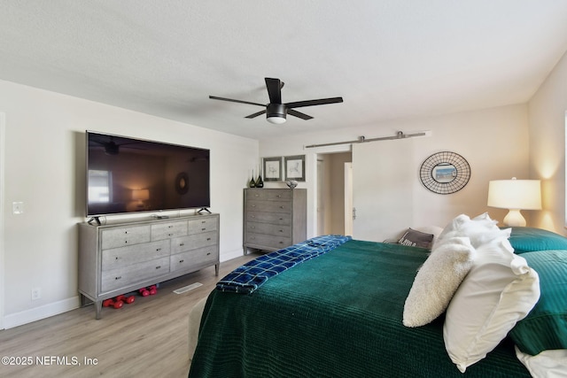 bedroom with hardwood / wood-style floors, ceiling fan, and a barn door