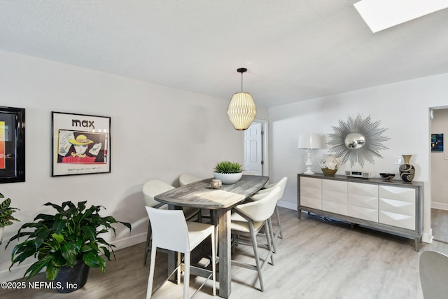 dining room featuring light wood-type flooring, a textured ceiling, and a skylight