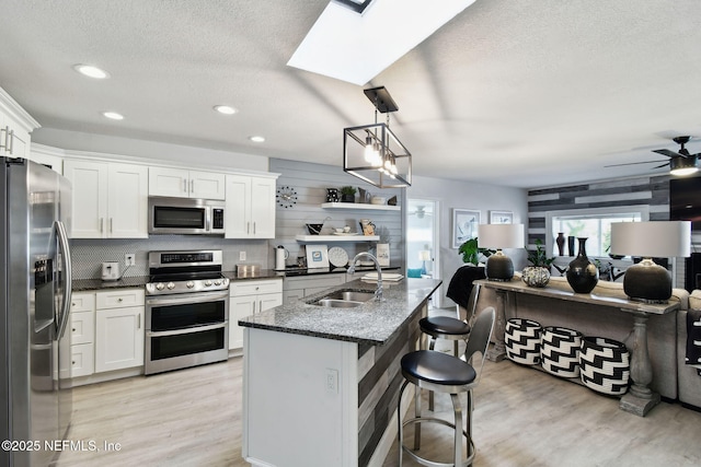 kitchen featuring appliances with stainless steel finishes, hanging light fixtures, a breakfast bar area, white cabinets, and sink