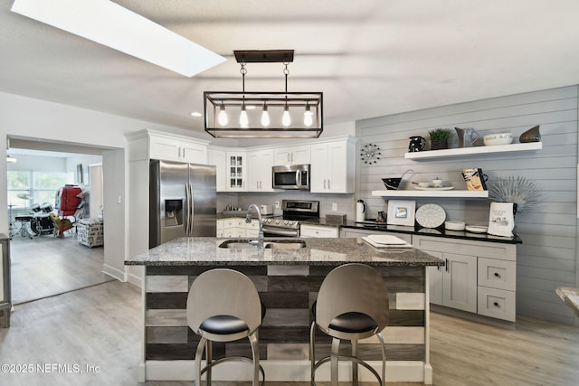 kitchen with a kitchen breakfast bar, stainless steel appliances, an island with sink, sink, and dark stone countertops