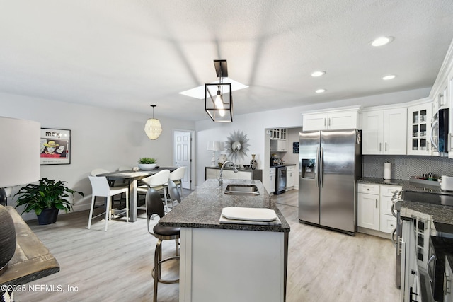 kitchen featuring hanging light fixtures, stainless steel appliances, sink, white cabinetry, and a kitchen island with sink