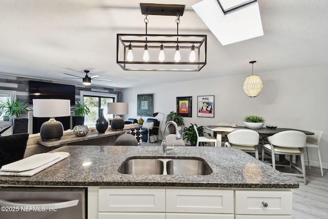 kitchen with white cabinetry, sink, dark stone counters, and decorative light fixtures