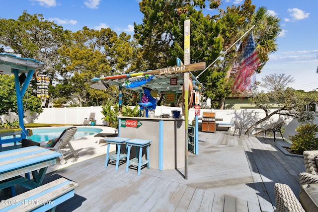 wooden terrace featuring exterior bar and a fenced in pool