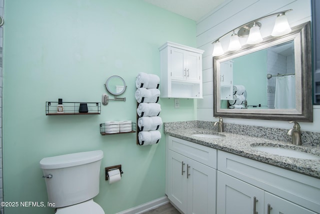 bathroom featuring double vanity, toilet, baseboards, and a sink