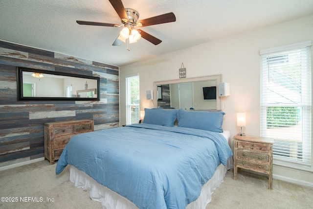 carpeted bedroom featuring multiple windows, a textured ceiling, an accent wall, and baseboards