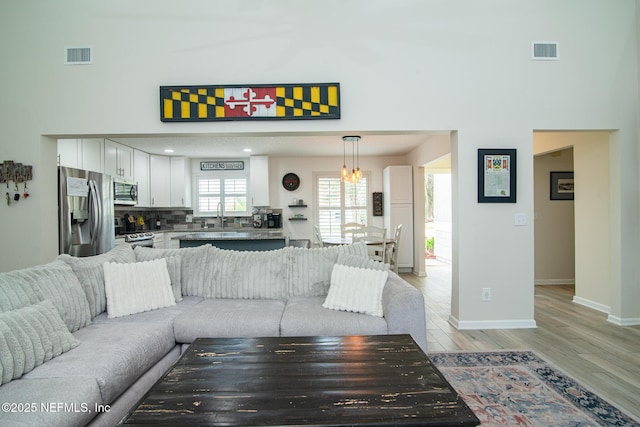 living area featuring a notable chandelier, visible vents, light wood-type flooring, and baseboards