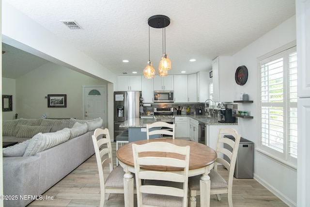 dining space with light wood-style flooring, plenty of natural light, visible vents, and a textured ceiling