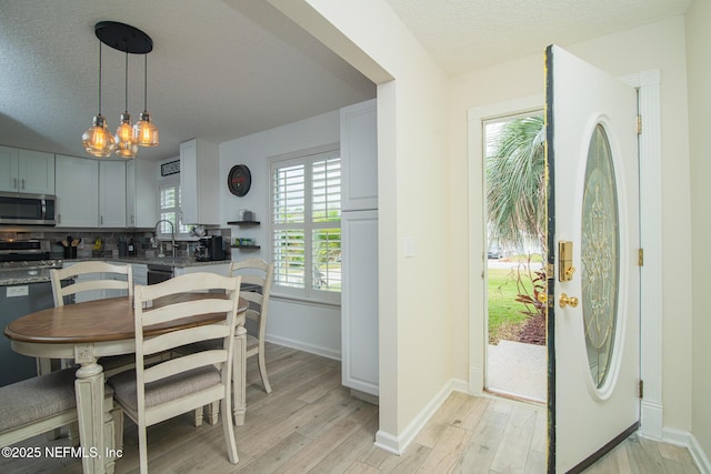 kitchen featuring light wood-type flooring, a sink, appliances with stainless steel finishes, a textured ceiling, and tasteful backsplash