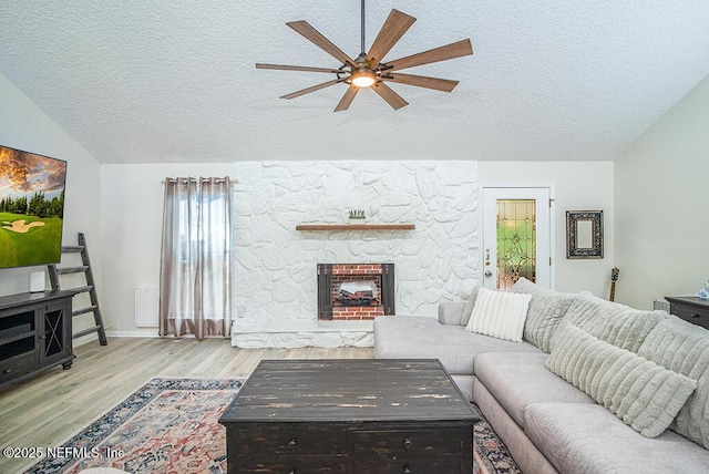 living area featuring wood finished floors, a ceiling fan, a stone fireplace, vaulted ceiling, and a textured ceiling