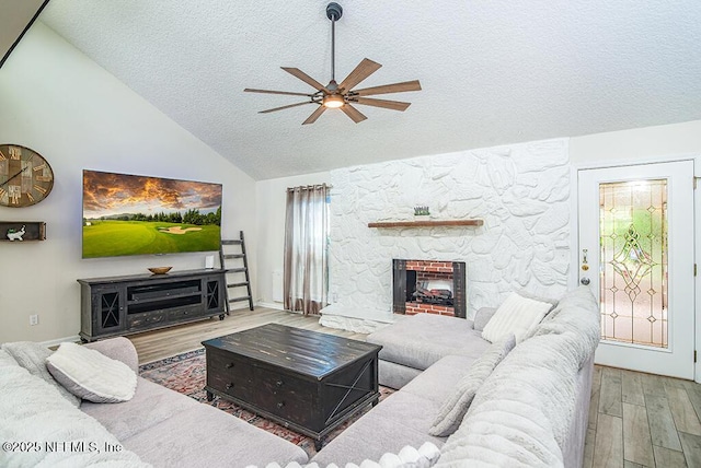 living room with wood finished floors, high vaulted ceiling, a fireplace, ceiling fan, and a textured ceiling