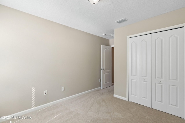 unfurnished bedroom featuring a textured ceiling, light colored carpet, visible vents, baseboards, and a closet