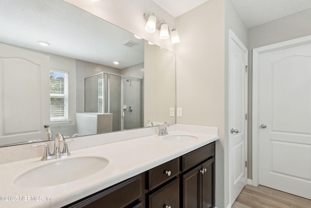 full bathroom with double vanity, wood finished floors, a sink, and a shower stall