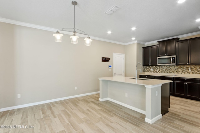 kitchen with a kitchen island with sink, a sink, visible vents, backsplash, and stainless steel microwave