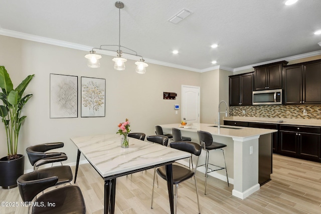 kitchen with tasteful backsplash, visible vents, stainless steel microwave, a kitchen breakfast bar, and a sink