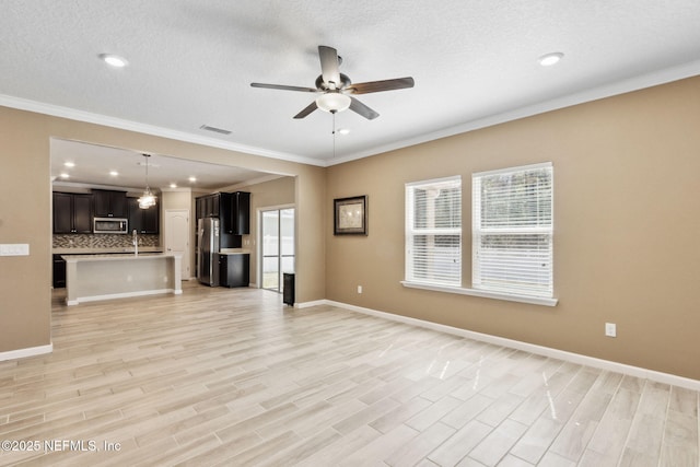 unfurnished living room featuring ceiling fan, a sink, visible vents, baseboards, and light wood-type flooring