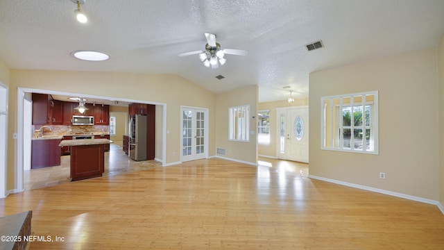 unfurnished living room with light wood finished floors, lofted ceiling, visible vents, a textured ceiling, and baseboards