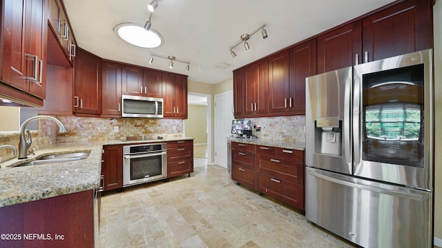 kitchen featuring light stone counters, a sink, appliances with stainless steel finishes, backsplash, and reddish brown cabinets