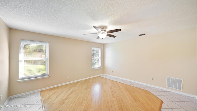 empty room featuring plenty of natural light, visible vents, and a ceiling fan