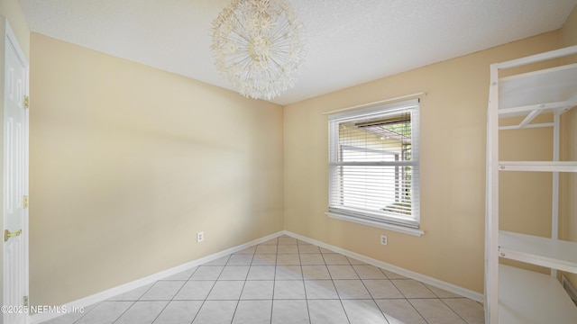 unfurnished room featuring a textured ceiling, baseboards, a notable chandelier, and light tile patterned flooring