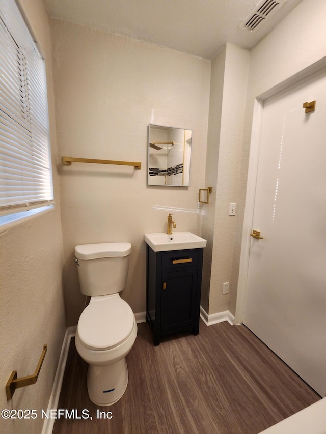 half bath featuring toilet, wood finished floors, vanity, visible vents, and baseboards