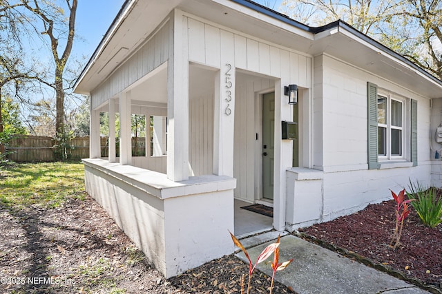 view of exterior entry with a porch and fence