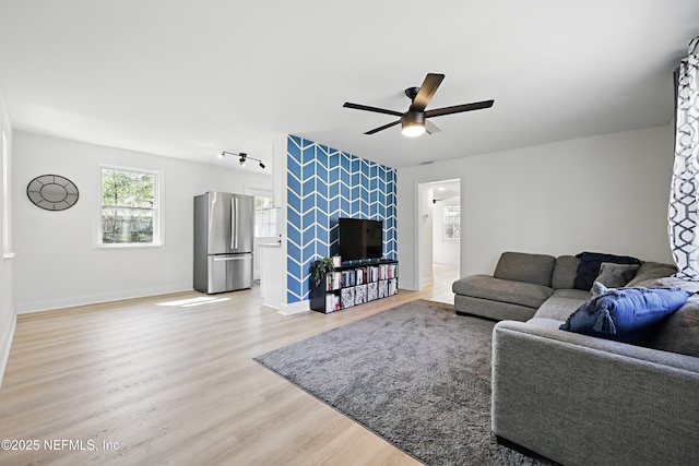 living room featuring light wood finished floors, baseboards, a ceiling fan, an accent wall, and track lighting