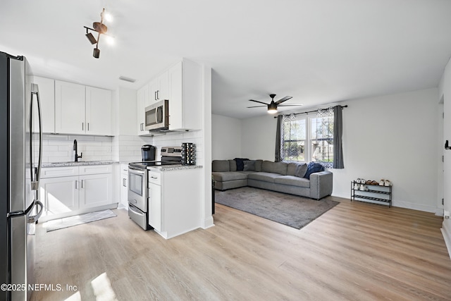 kitchen with stainless steel appliances, light wood-type flooring, white cabinets, and tasteful backsplash