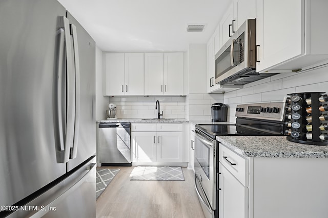 kitchen with visible vents, decorative backsplash, appliances with stainless steel finishes, light wood-type flooring, and a sink