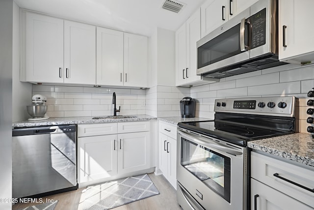 kitchen featuring visible vents, white cabinets, appliances with stainless steel finishes, light stone counters, and a sink