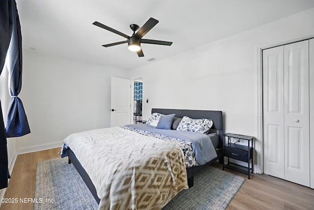 bedroom featuring wood finished floors, visible vents, baseboards, a ceiling fan, and a closet