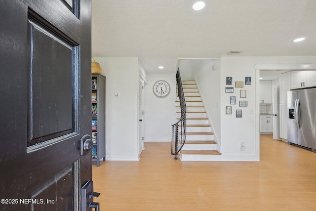 entryway featuring light wood-type flooring, stairway, baseboards, and visible vents