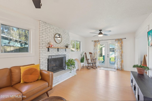 living room featuring wood finished floors, a brick fireplace, a ceiling fan, and french doors