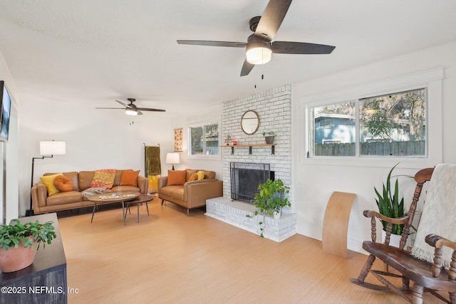 living area with wood finished floors, a brick fireplace, a ceiling fan, and a healthy amount of sunlight