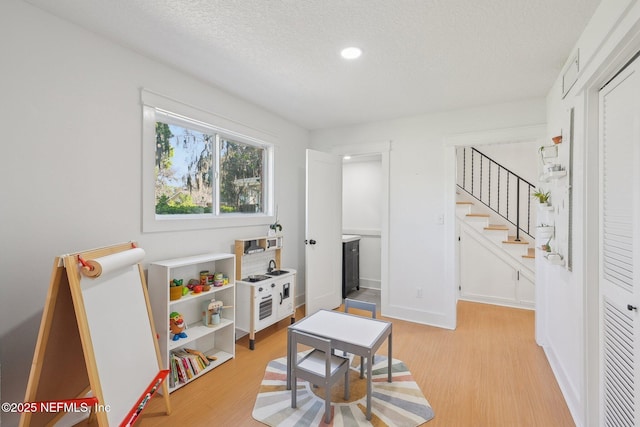 game room with baseboards, light wood-style floors, and a textured ceiling