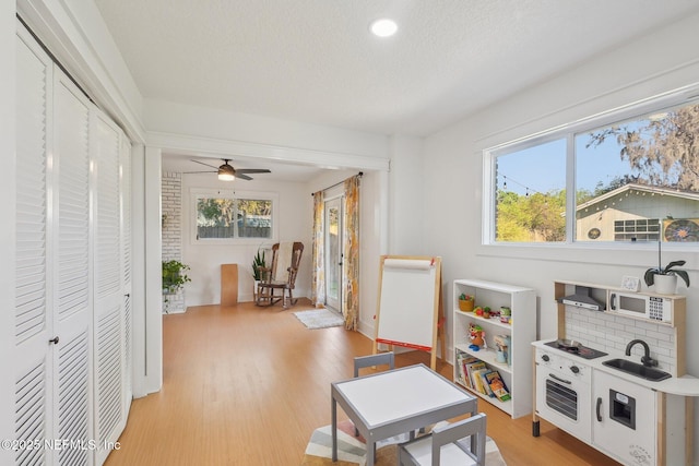 rec room featuring a sink, light wood-style floors, ceiling fan, and a textured ceiling