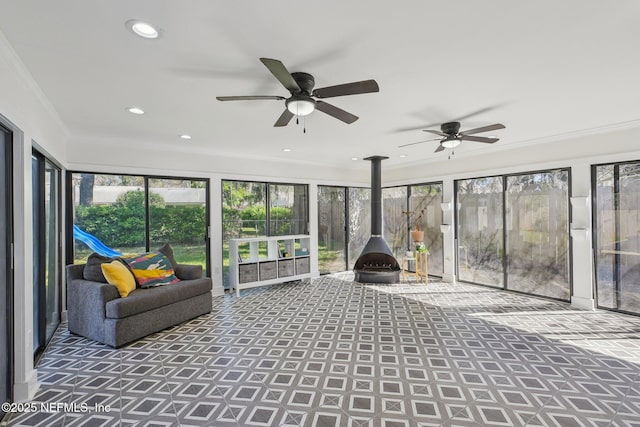 unfurnished sunroom featuring a wood stove and ceiling fan