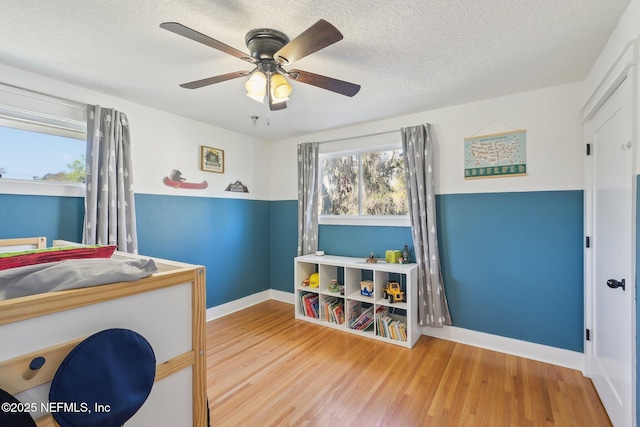 bedroom featuring baseboards, a textured ceiling, a ceiling fan, and wood finished floors