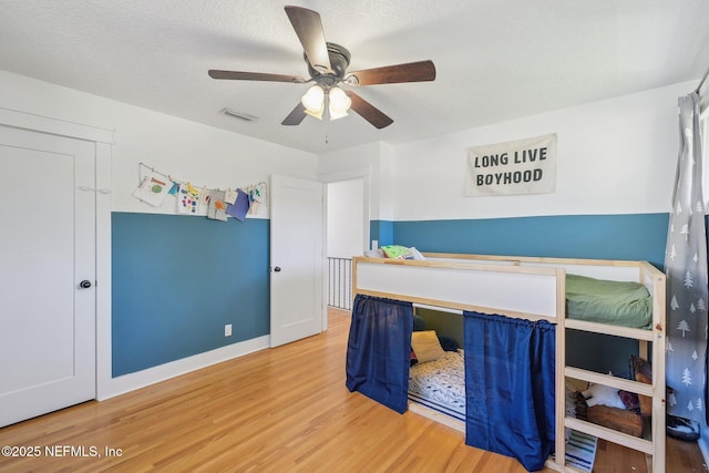 bedroom featuring ceiling fan, visible vents, a textured ceiling, and wood finished floors