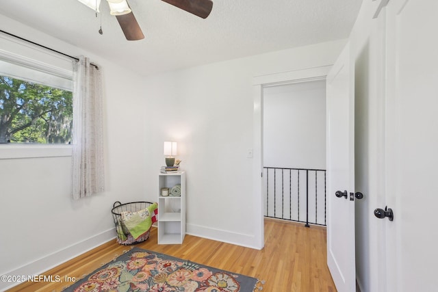 sitting room with light wood finished floors, a textured ceiling, baseboards, and ceiling fan