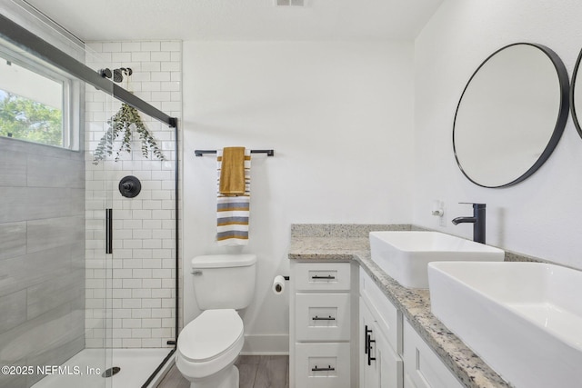 full bath with double vanity, toilet, a stall shower, and a sink