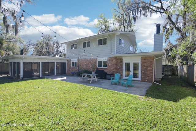 rear view of property featuring a lawn, fence, french doors, brick siding, and a patio area