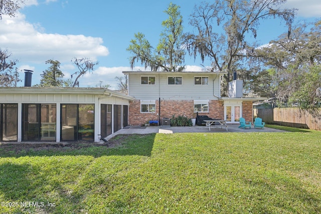 back of house featuring brick siding, fence, a lawn, a sunroom, and a patio area