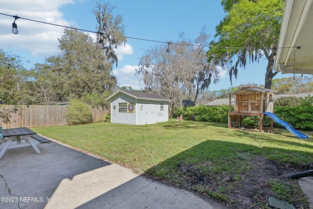 view of yard featuring a patio area, fence, an outbuilding, and a playground