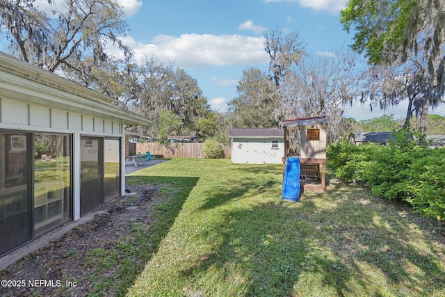 view of yard with fence, an outdoor structure, a storage shed, and a playground