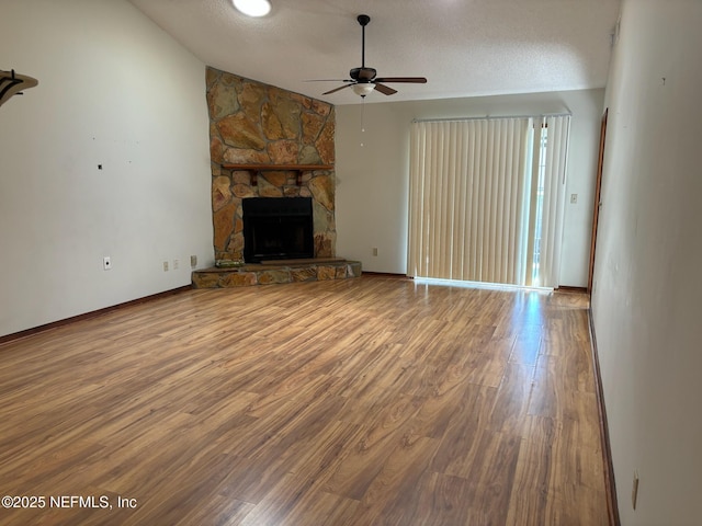 unfurnished living room featuring a textured ceiling, hardwood / wood-style flooring, a stone fireplace, and lofted ceiling