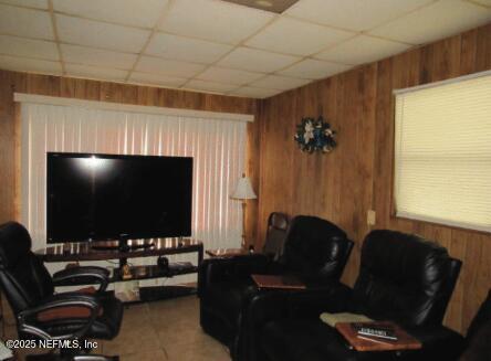 living area with a paneled ceiling and wooden walls