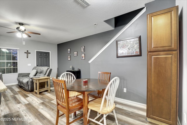 dining area featuring light wood-type flooring, visible vents, a textured ceiling, and baseboards