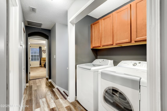 laundry area with cabinet space, visible vents, light wood-style flooring, washing machine and clothes dryer, and a textured ceiling