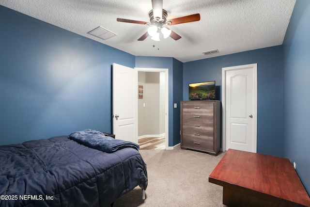 bedroom with a ceiling fan, visible vents, light carpet, and a textured ceiling