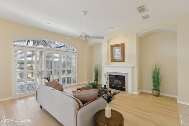 living room featuring light hardwood / wood-style floors, a tile fireplace, and ceiling fan